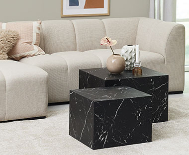 Kaksi kuution mallista sohvapöytää mustalla marmoriefektillä sekä muhkea beige sohva olohuoneessa