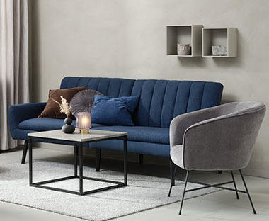 Sininen vuodesohva, betonijäljitelty sohvapöytä ja harmaa nojatuoli