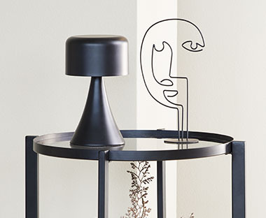 Muotoiltu veistos sivupöydällä mustan paristokäyttöisen lampun vieressä