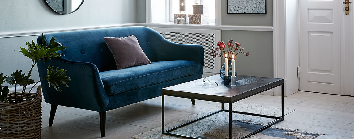 Olohuoneessa sininen samettisohva ja sohvapöytä, jossa kynttilät