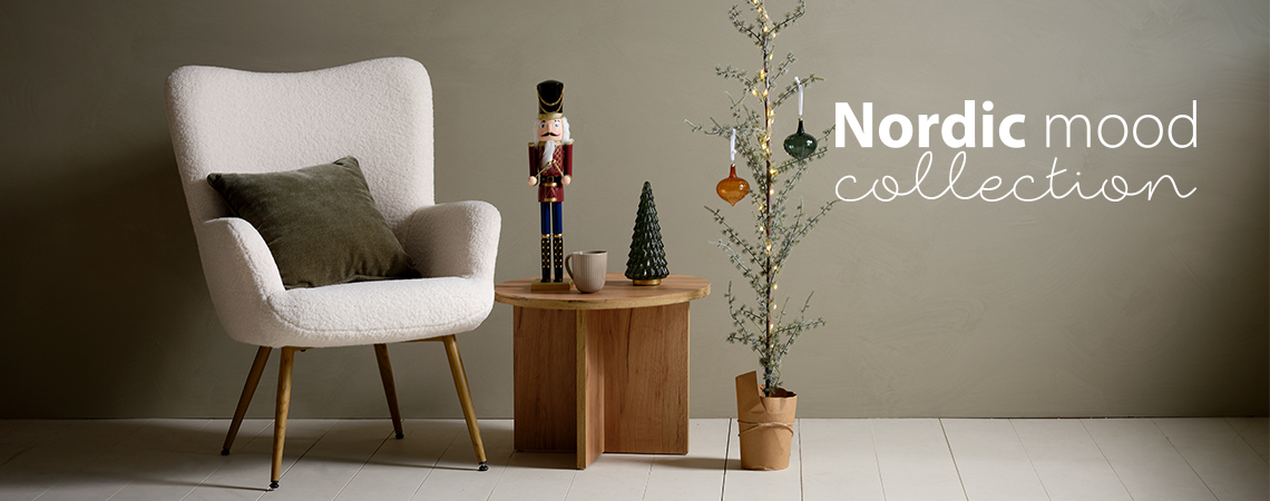 Nojatuoli, jossa on tyyny, sohvapöytä, jossa on jouluhahmo ja ohut joulukuusi, joka on koristeltu lasipalloilla