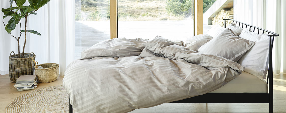 Makuuhuone, jossa musta metallisänky, peitot ja tyynyt, peiteltynä vaaleanharmaalla ja valkoisella raidallisilla vuodevaatteilla