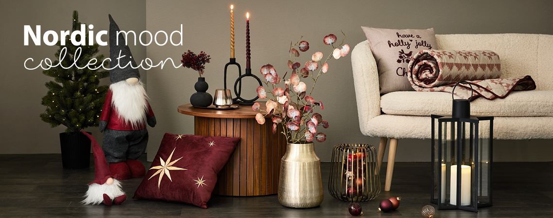 Joulutontut, tyynyt, kultainen maljakko tekokukalla, kultainen kynttilänjalka ja musta lyhty valkoisen sohvan edessä