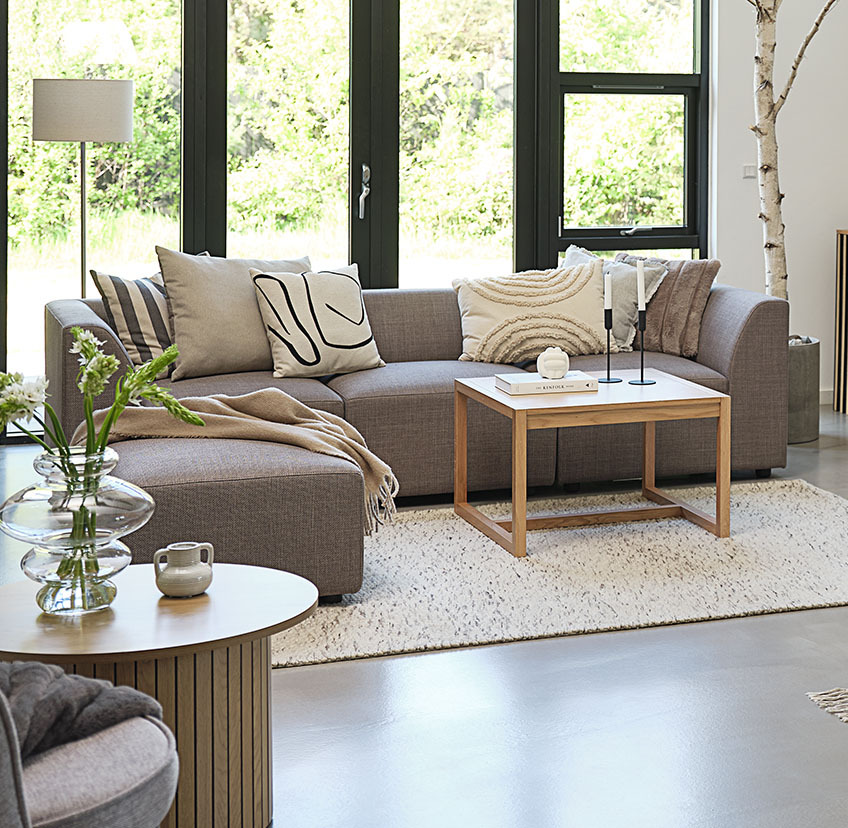 Minimalistinen tamminen sohvapöytä valoisassa olohuoneessa isolla sohvalla ja koristetyynyillä