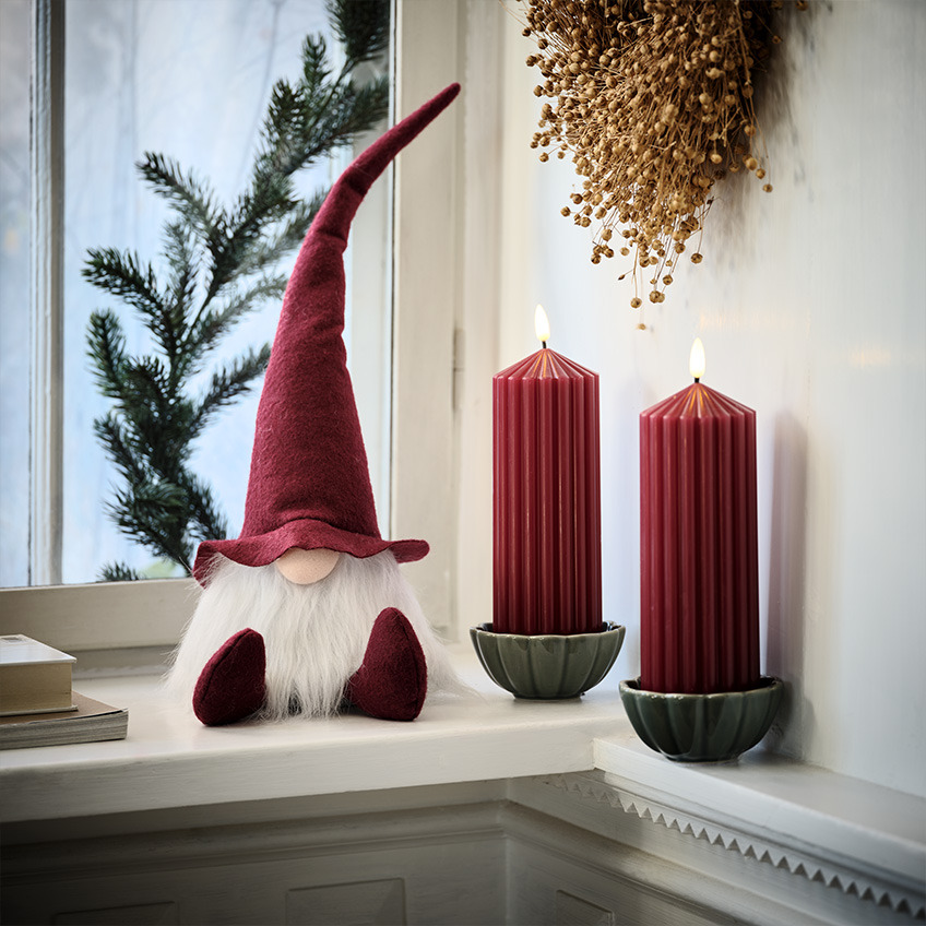 Skandinaavinen joulutonttu ikkunalaudalla suurten punaisten kynttilöiden vieressä