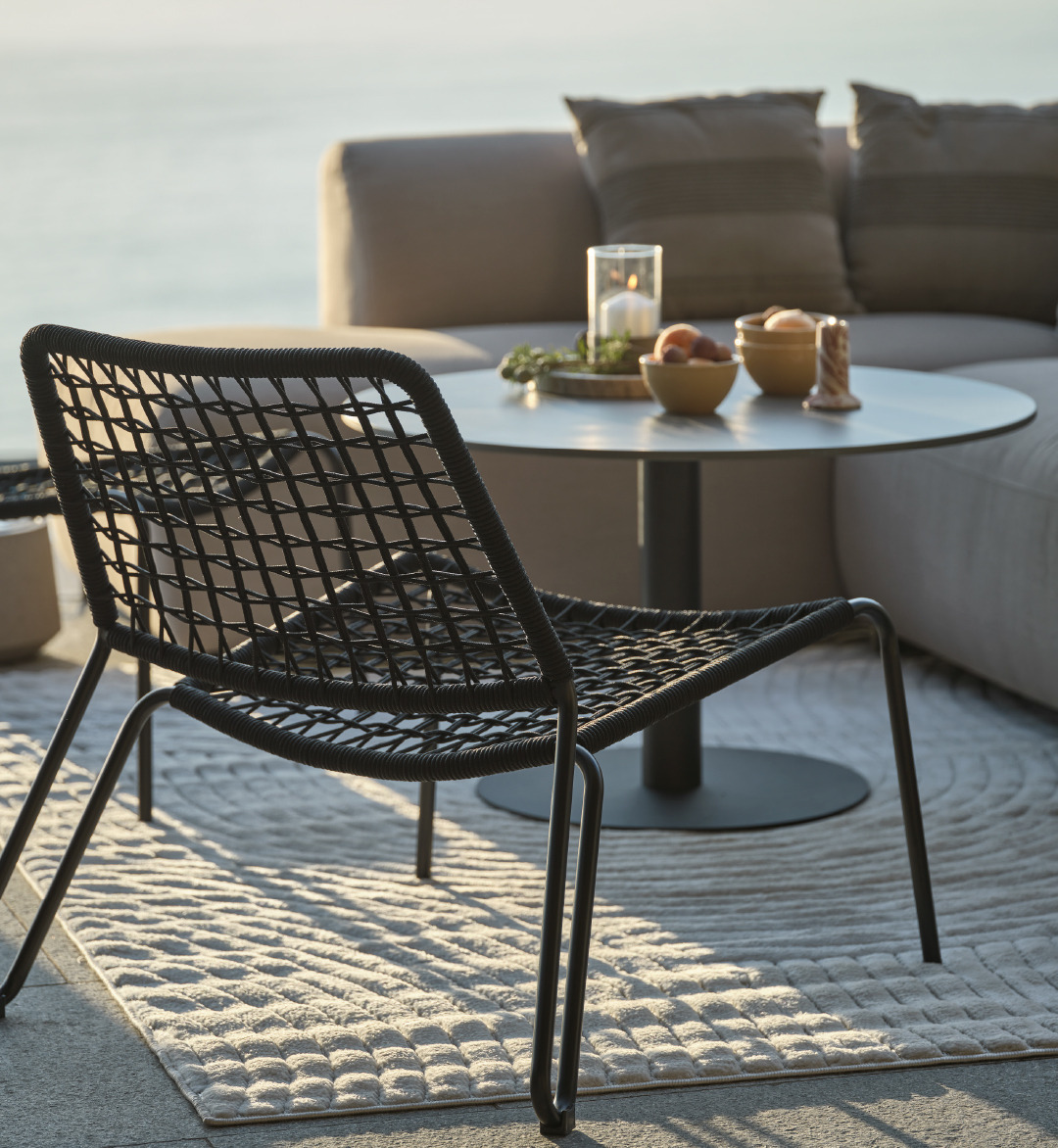 Puutarhasohva aurinkoisella terassilla, musta puutarhatuoli ja pyöreä loungepöytä