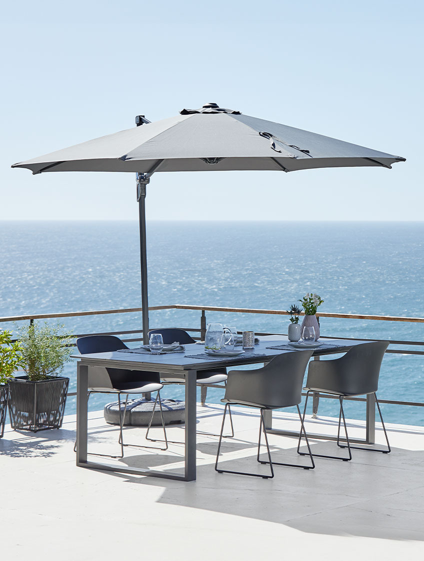 Suuri riippuvarjo ja puutarhapöytä sekä -tuolit terassilla meren ääressä