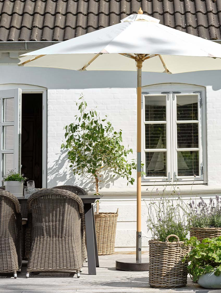 Klassinen luonnonvalkoinen aurinkovarjo terassilla puutarhapöydän ja -tuolien kanssa