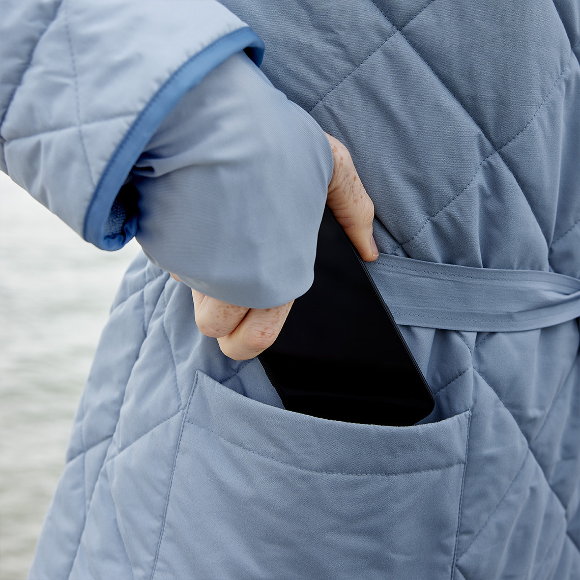 OSBY-kylpytakissa on isot sisä- ja ulkotaskut Henkilö laittamassa puhelinta kylpytakin taskuun