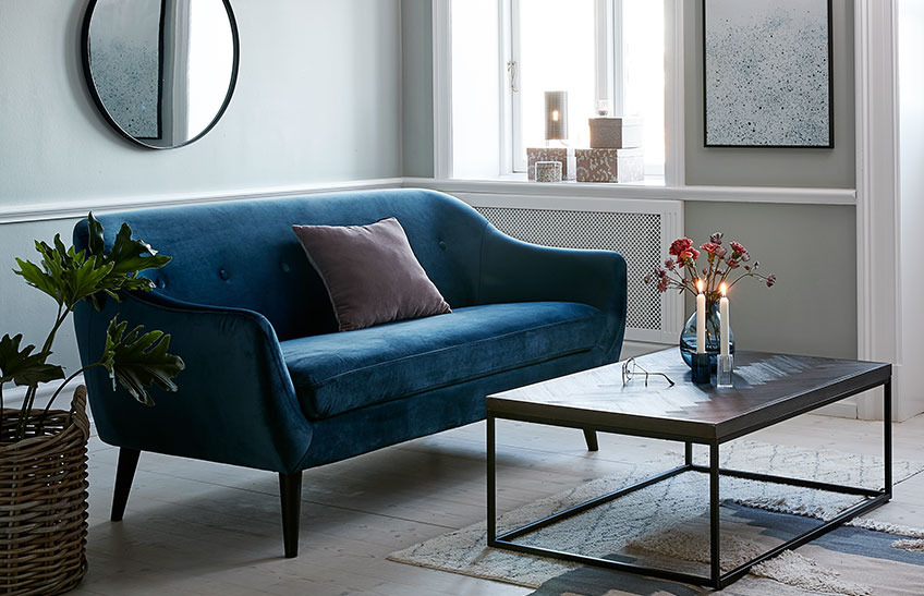 Olohuone, jossa sininen samettinen sohva ja sohvapöytä