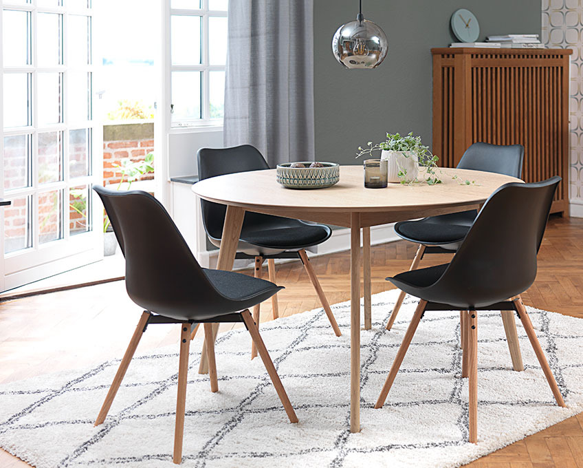 Round dining table and black dining chairs on a rug in a dining room
