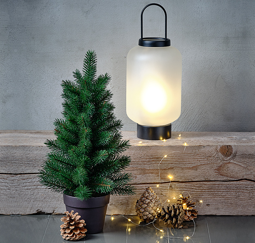 Artificial Christmas tree, glass lantern with frosted look and a light string wrapped over a log 