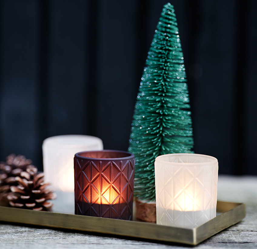 Tea light holders in glass on a metal tray with small Christmas tree and pinecones 