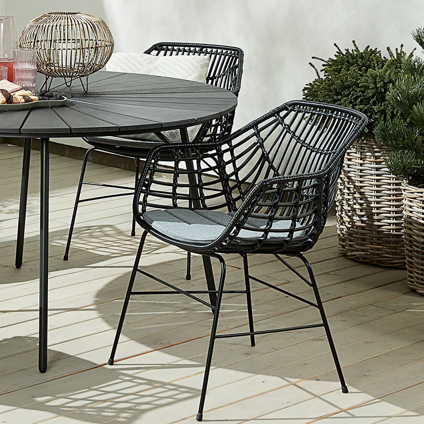 Black polyrattan garden chair with a round garden table on a patio