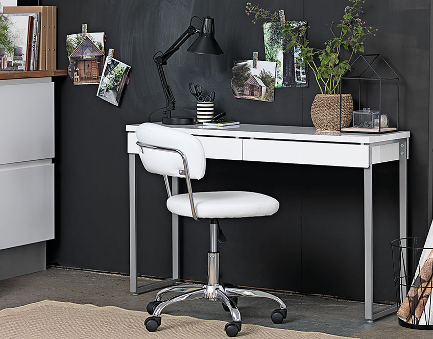 Small white desk with drawers and a white office chair by a black wall 
