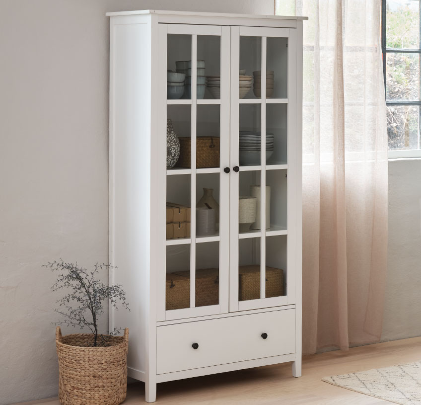 White cabinet with glass doors by the window in a light room 