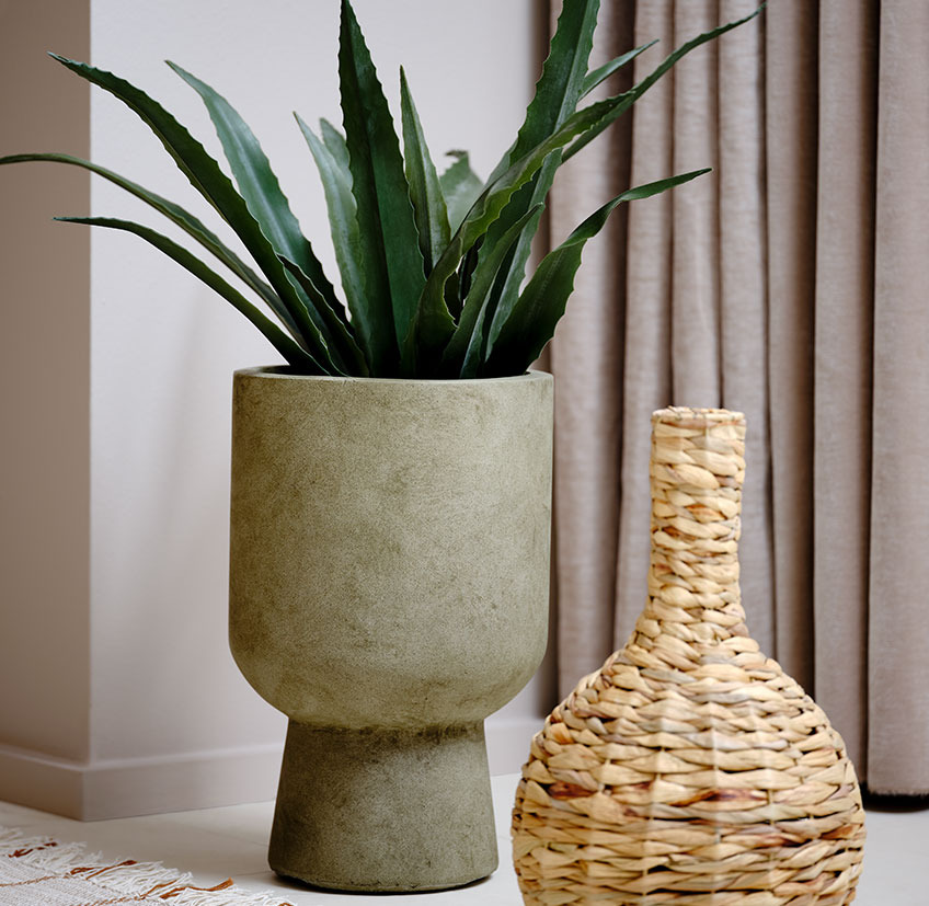 Green plant pot with artificial plant next to a wicker vase  