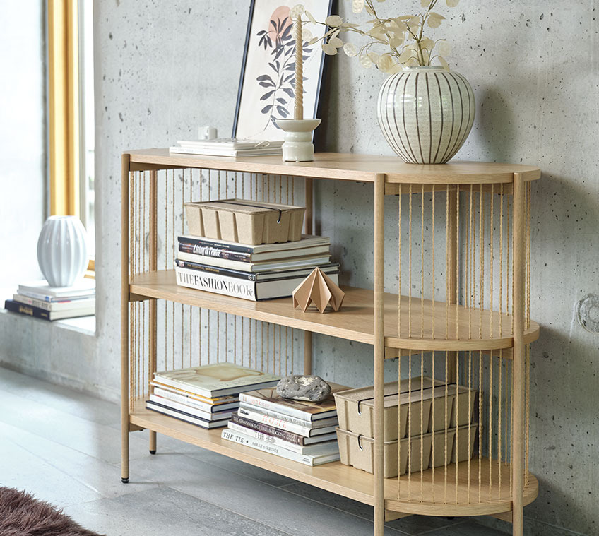 Living room with a light oak sideboard with a vase on top and books and storage boxes on the shelves