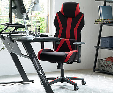 Punamusta pelituoli pyörillä ja työpöytä sekä näytön jalusta parempaan työskentelymukavuuteen ja ergonomiaan