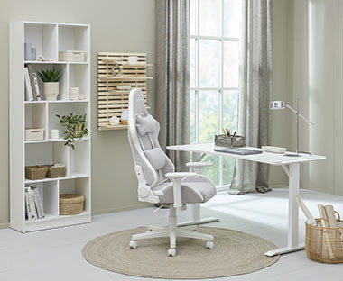 Tyylikäs valkoinen pelituoli, valkoinen korkeussäädettävä työpöytä ja valkoinen kirjahylly työhuoneessa